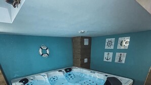 Kylpyhuone, jossa on suuri kylpyamme, pieni ikkuna ja merellisteemaisia seinäkoristeita.