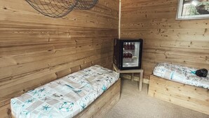 Puuinen mökki, jossa on kaksi puista sänkyä, kattoverkko ja pieni jääkaappi.