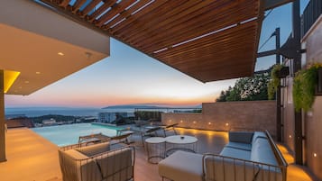 Ein moderner Außenbereich zum Entspannen mit Pool, Sitzgelegenheiten und Blick auf den Sonnenuntergang über dem Meer.