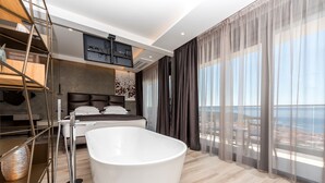 A modern bedroom with a large bathtub, a bed, and a view of the sea.