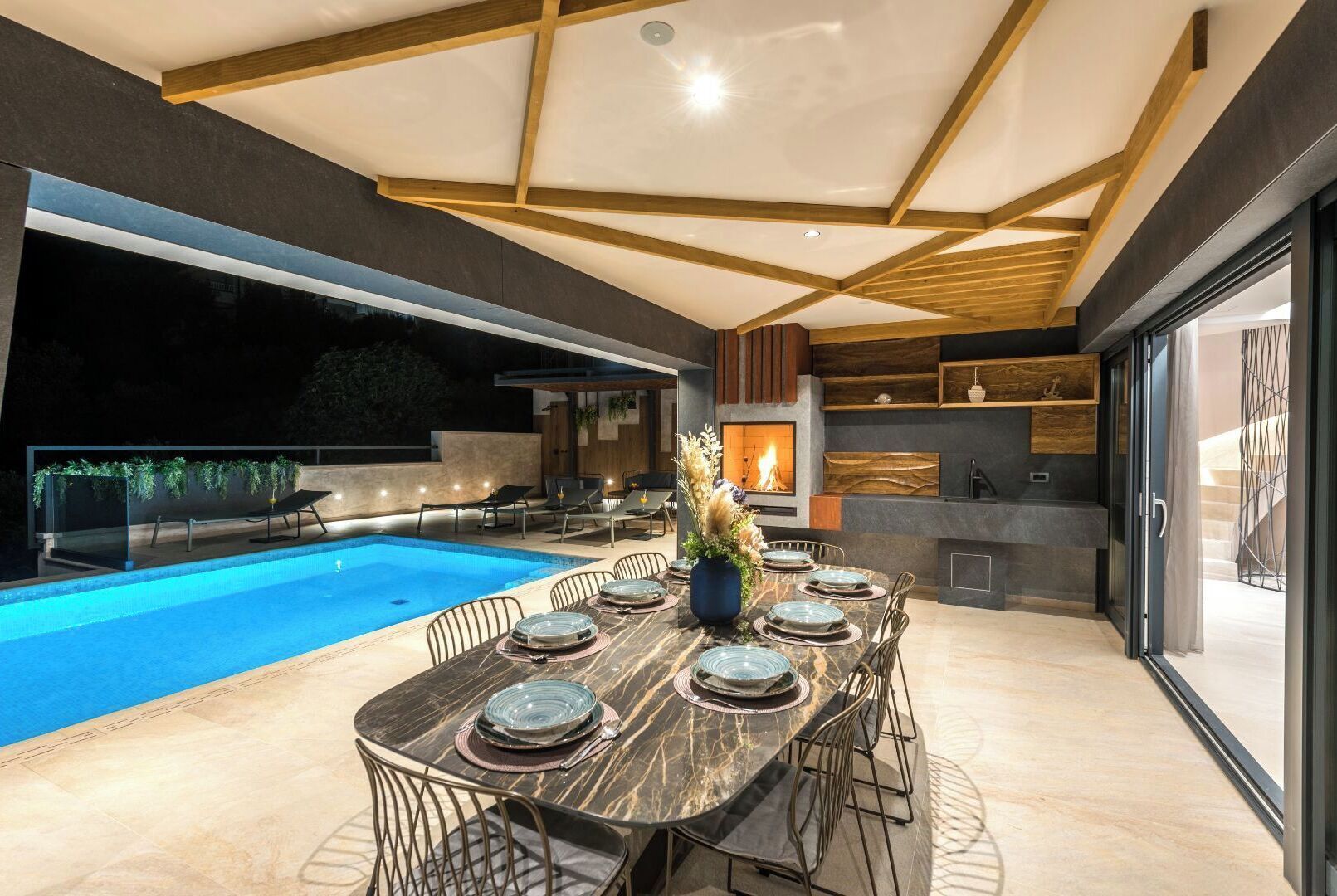 Ein moderner Außenbereich mit Essplatz, Pool, Feuerstelle und Küchenbereich mit Steinrückwand.