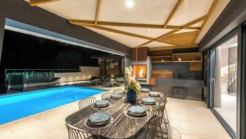 Ein moderner Außenbereich mit Essplatz, Pool, Feuerstelle und Küchenbereich mit Steinrückwand.