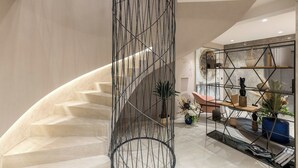 A modern interior with a curved staircase, a decorative metal railing, and a wooden bookshelf with various items.