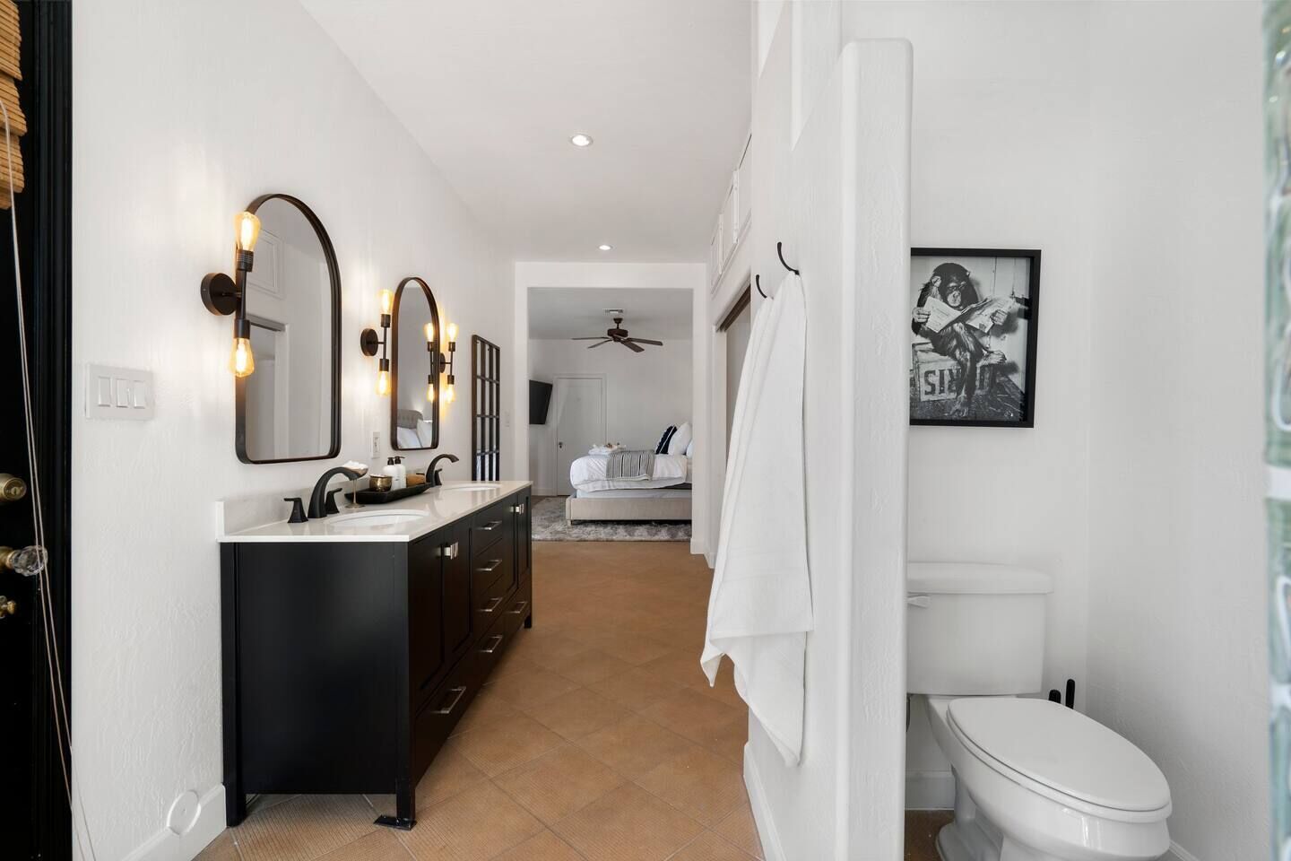 A modern bathroom with a black vanity, two mirrors, and a ceiling fan.