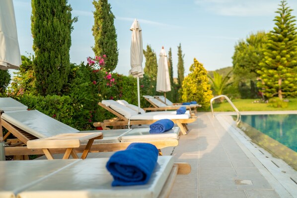 A poolside area with sun loungers, a pool, and surrounding greenery.