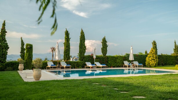 A pool area with lounge chairs and umbrellas, surrounded by greenery and tall trees. - Kos Secret Villa with private pool (Kos)