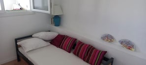 A small, single-bed room with a wooden frame, white bedding, and striped pillows.