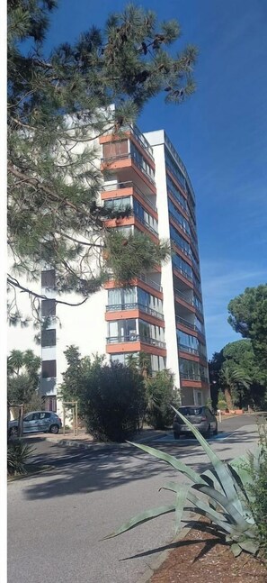 A multi-story residential building with balconies, surrounded by trees and parked cars.