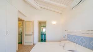 A bedroom with a bed, a nightstand, a wall-mounted lamp, and a bathroom visible through an open door. - Casa Lola by Wonderful Italy (Olbia)
