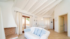 A spacious living area with a white sofa, a fireplace, and a dining area with a table and chairs. - Casa Lola by Wonderful Italy (Olbia)