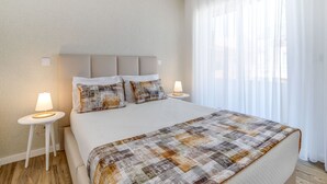 A neatly made bed with a quilt, two bedside tables with lamps, and sheer curtains. - Oceanfront 3BR Apt 20m from calm Beach (Póvoa de Varzim)