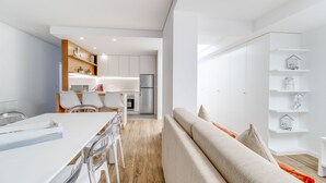 A modern kitchen with white cabinets, a dining area with a white table and chairs, and a living area with a sofa and shelves. - Oceanfront 3BR Apt 20m from calm Beach (Póvoa de Varzim)