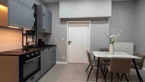 A modern kitchen with grey cabinets, a black stove, and a dining area with a white table and chairs. - **** * Designer Apartment 18th (TOP 1) (Wien)