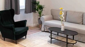 A living room with a dark green armchair, a light-colored sofa, a round coffee table, and a potted plant with yellow flowers. - **** * Designer Apartment 18th (TOP 1) (Wien)