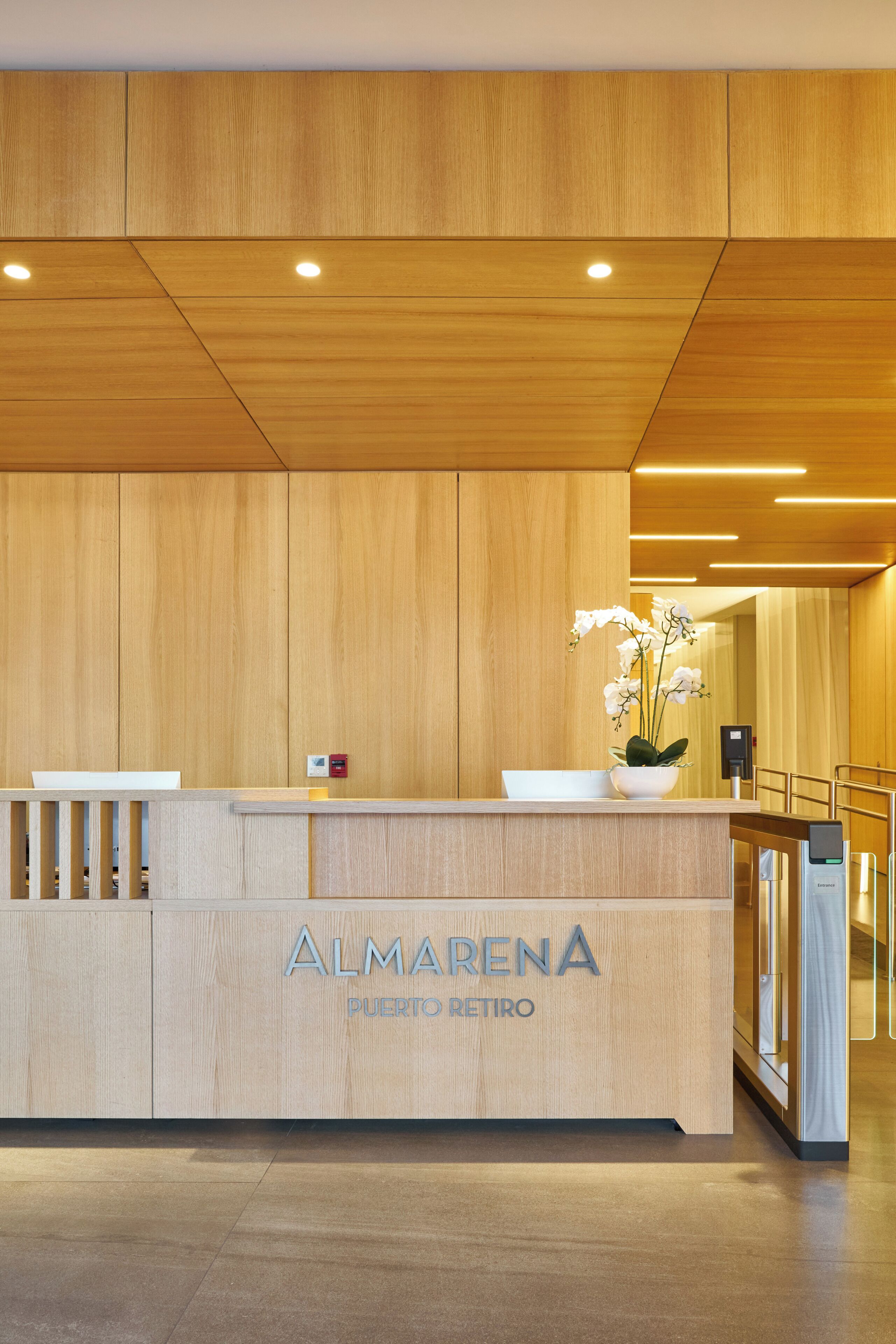 A reception desk with a wooden finish, a white flower vase, and the name "ALMARENA PUERTO RETIRO" on it.