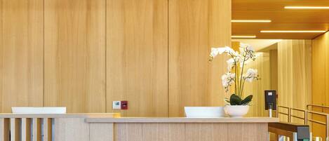 A reception desk with a wooden finish, a white flower vase, and the name "ALMARENA PUERTO RETIRO" on it.