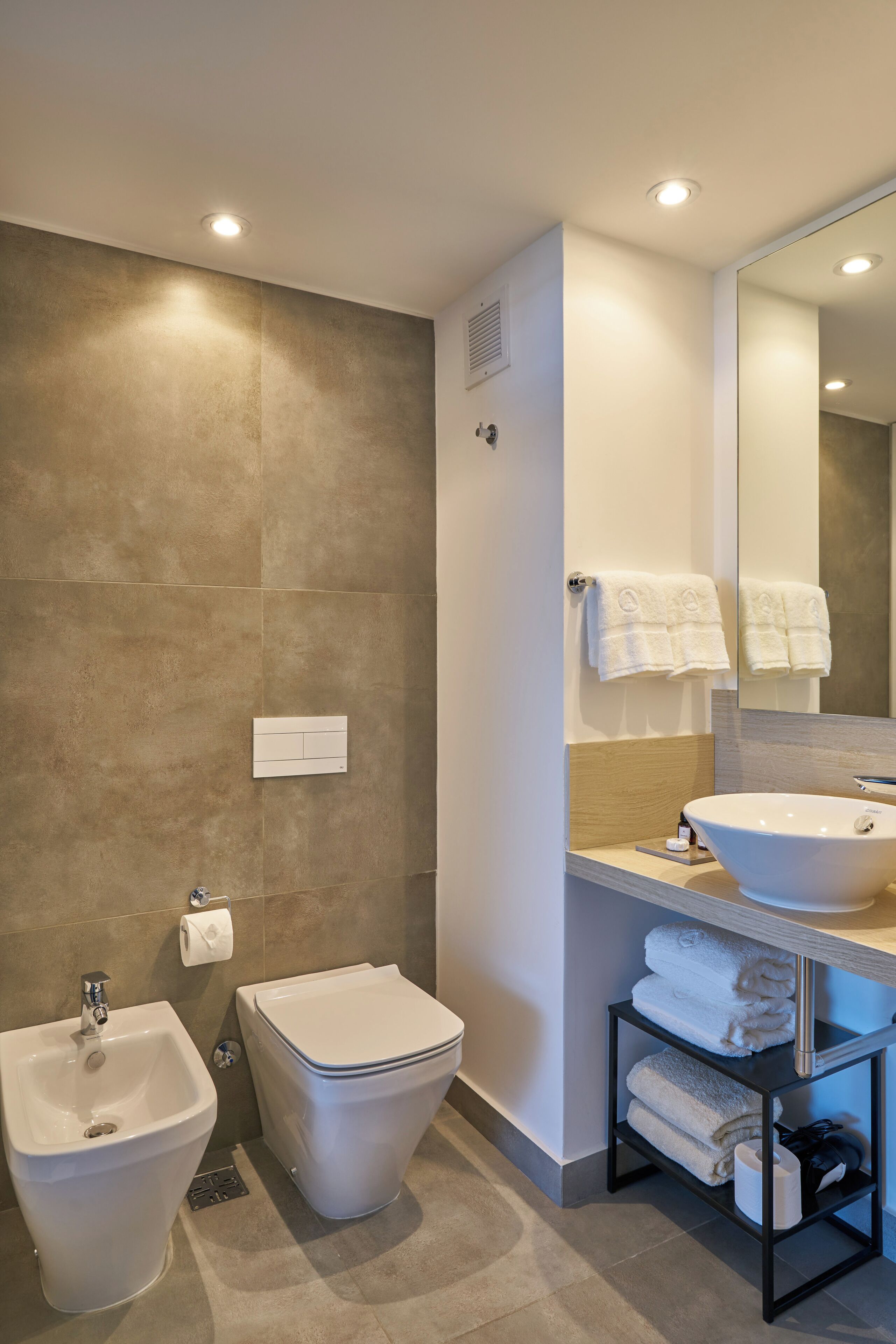 A modern bathroom with a bidet, toilet, sink, and a large mirror.