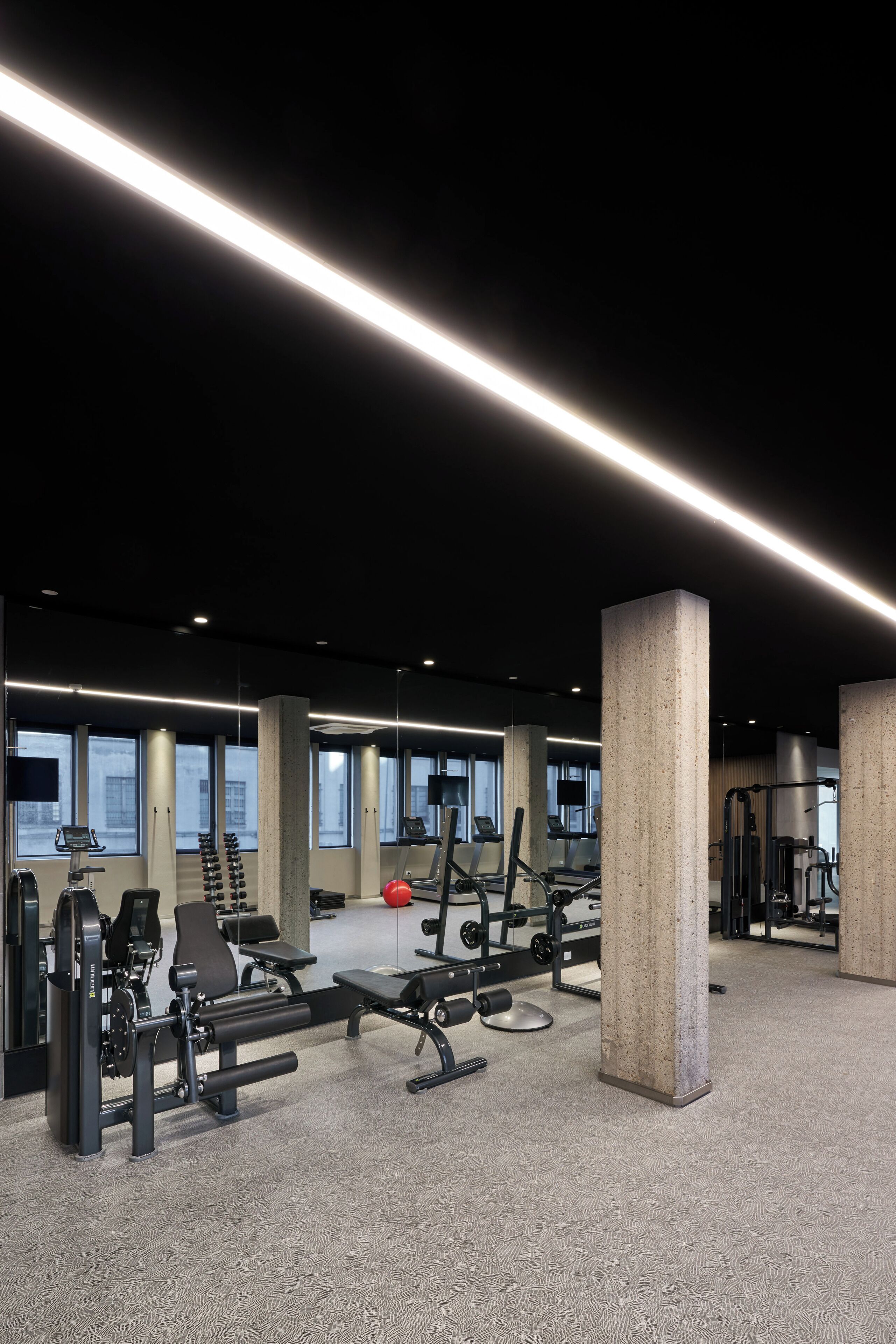 Ett gym med träningsutrustning, stora fönster och betongpelare.