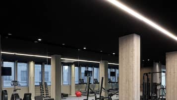 Ett gym med träningsutrustning, stora fönster och betongpelare.