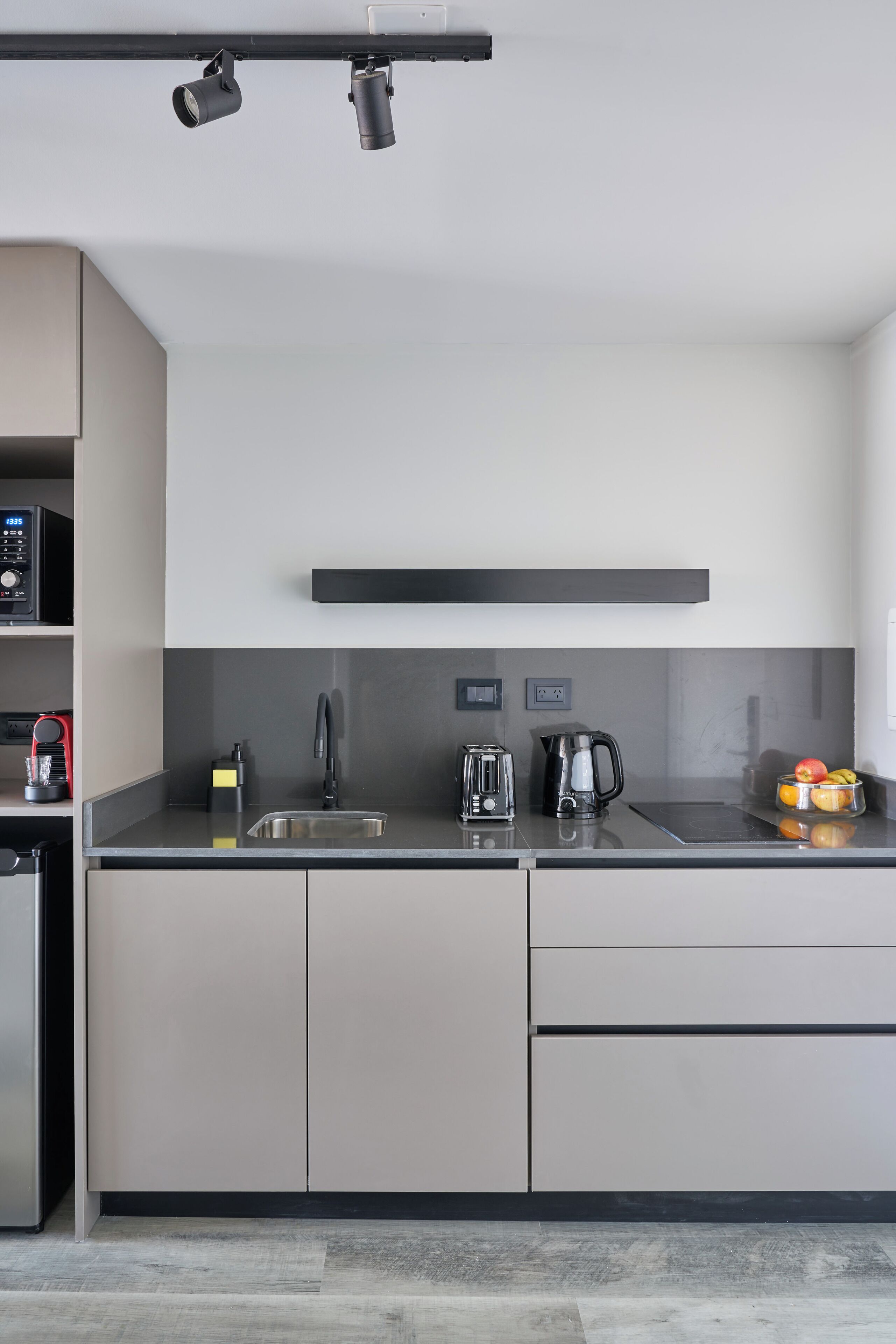 A modern kitchen with a stainless steel sink, a kettle, and a fruit bowl on the counter.