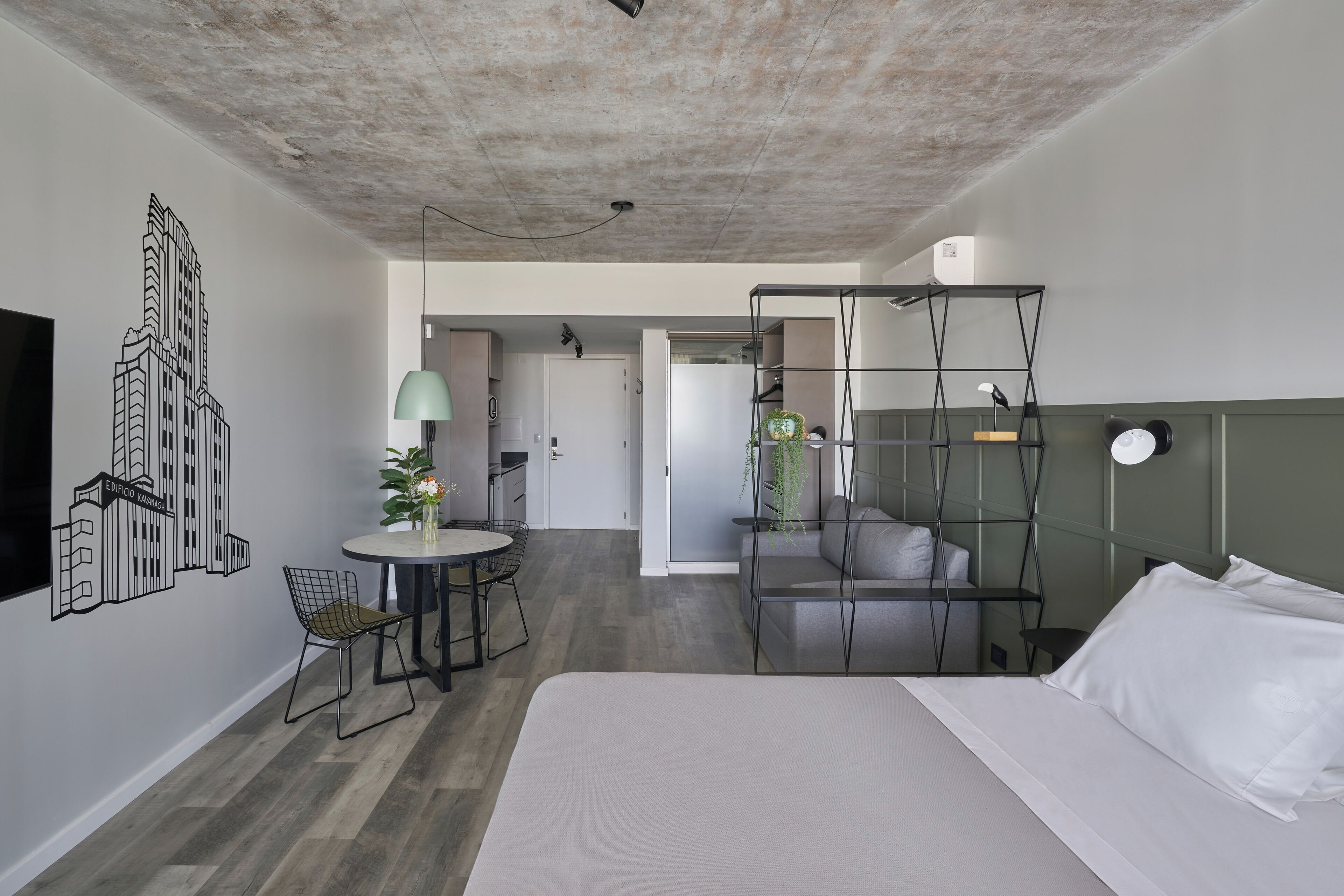 Una moderna camera d'albergo con un letto grande, un'area pranzo con tavolo e sedie, una kitchenette e un soggiorno con divano e televisore.