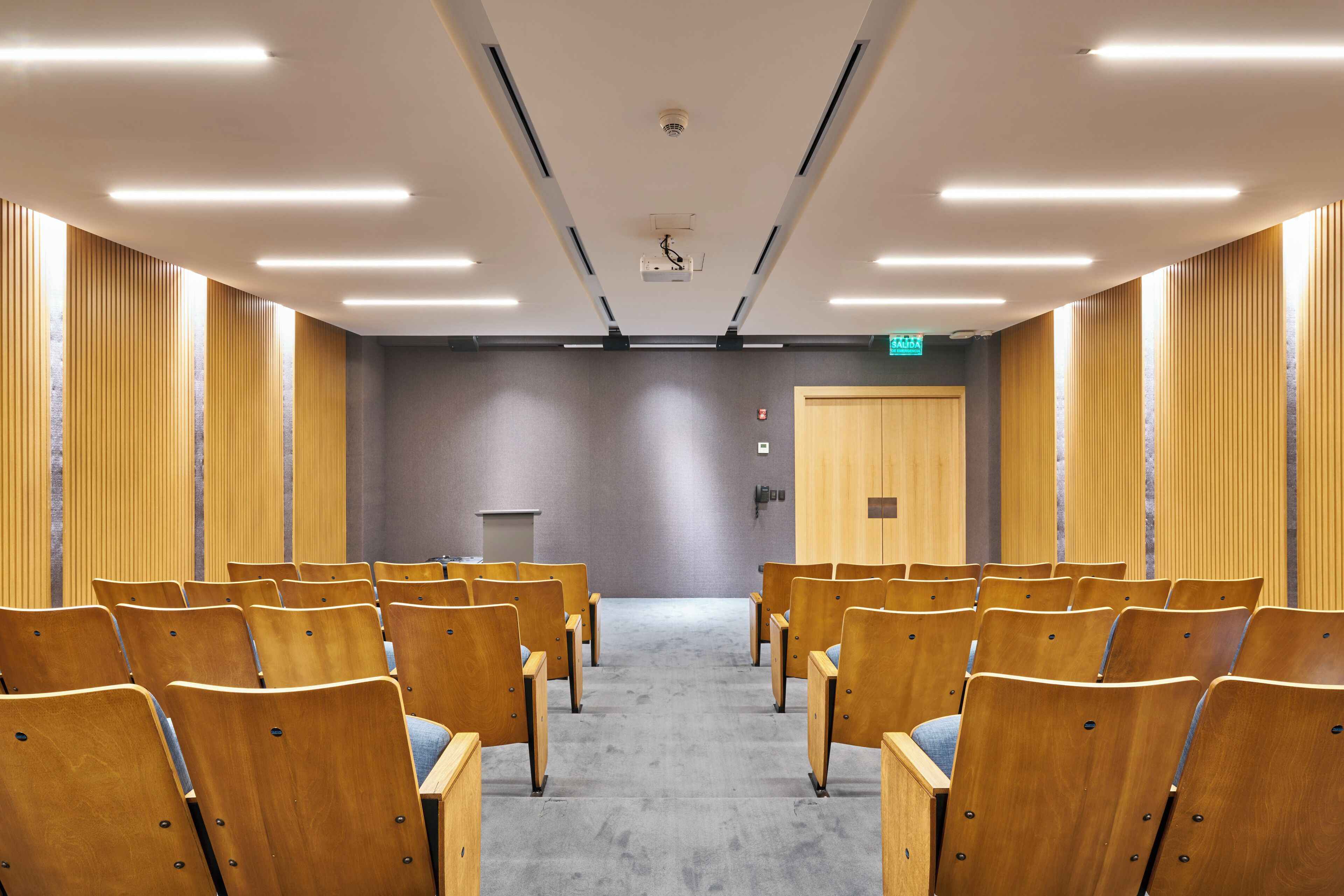 Une salle de conférence avec des rangées de chaises en bois, un pupitre et un tapis gris.