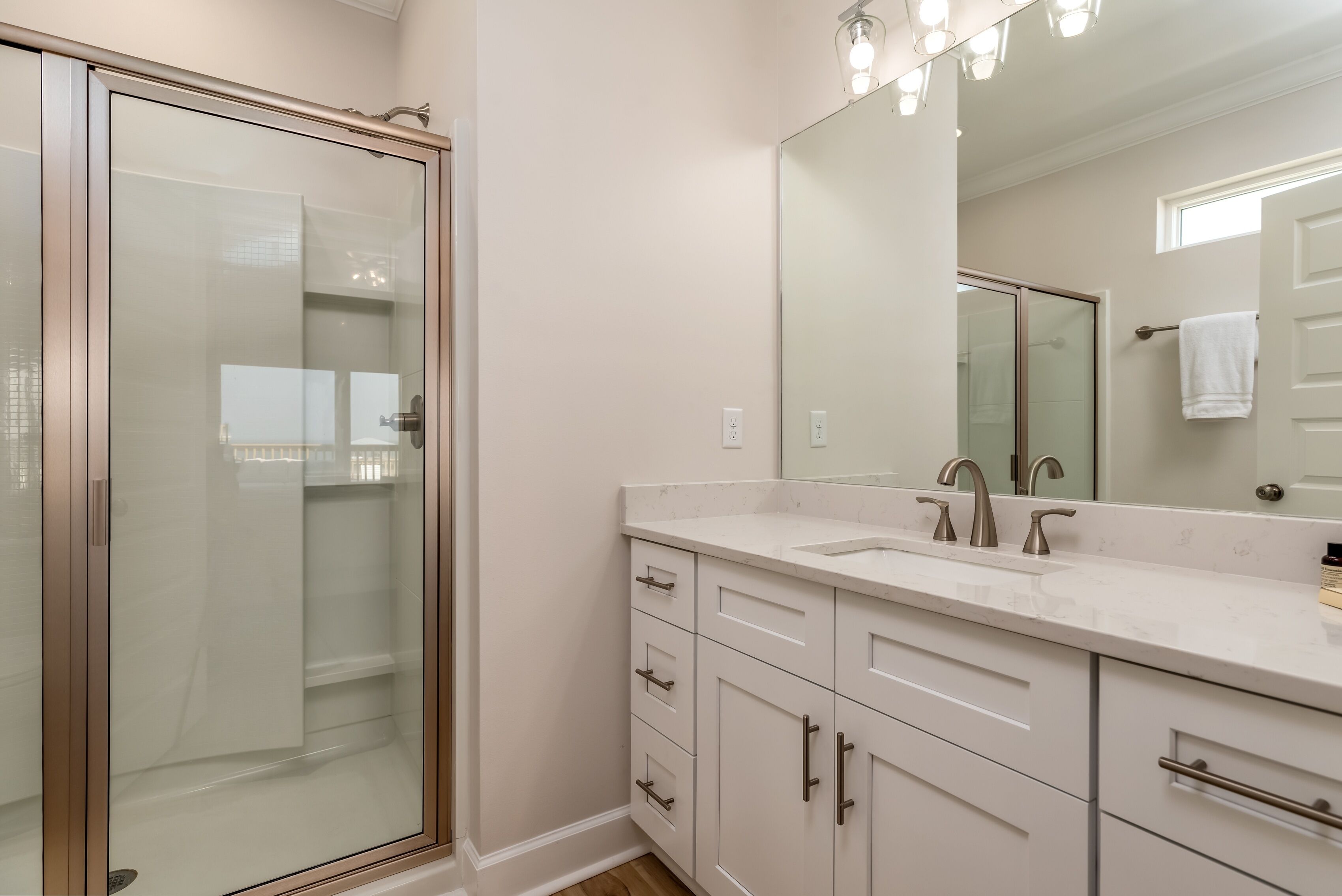 A modern bathroom with a glass shower enclosure, a large mirror, and white cabinetry.