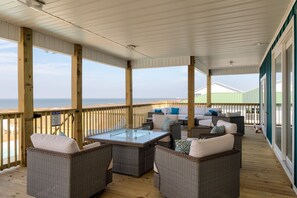A covered outdoor seating area with wicker furniture and a glass-top table, overlooking a beach. - Until Nextime - 2712 Bienville 5 Bedroom Home by RedAwning (Dauphin Island)