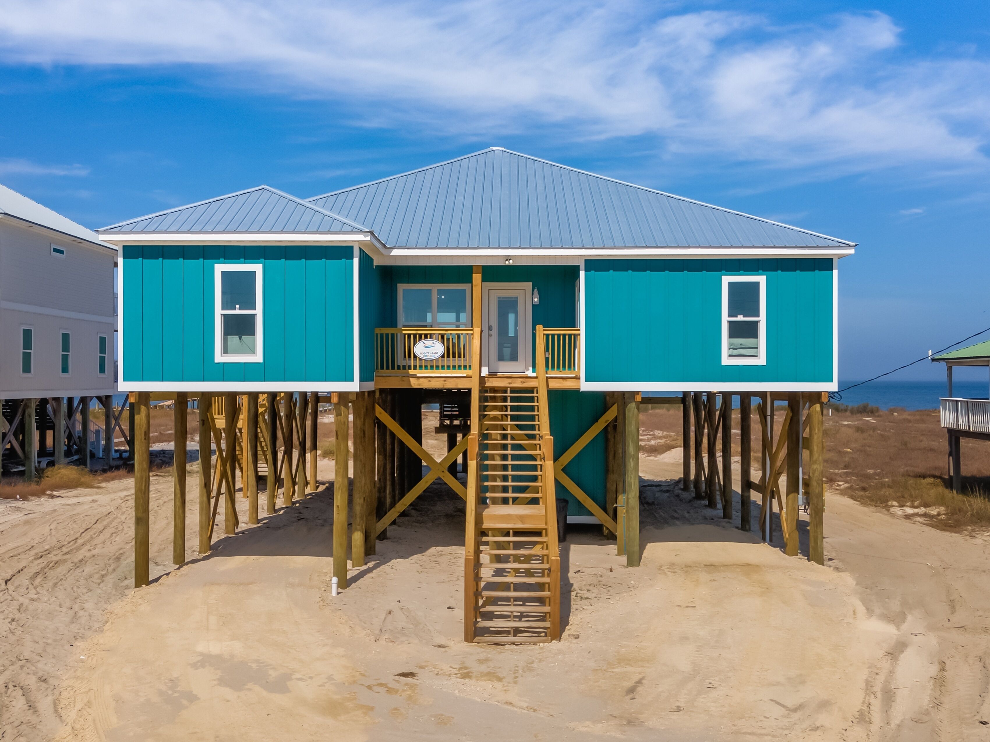 A two-story beach house with a wooden deck and a staircase leading to the entrance.