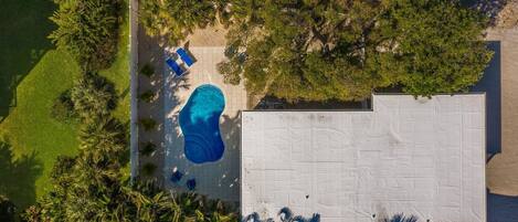 An aerial view of a property with a swimming pool, a covered patio area, and surrounding greenery.
