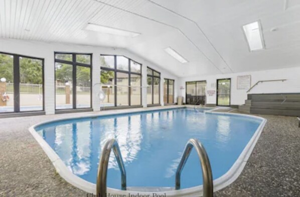 An indoor swimming pool with clear glass walls, a tiled floor, and a ceiling with recessed lighting.