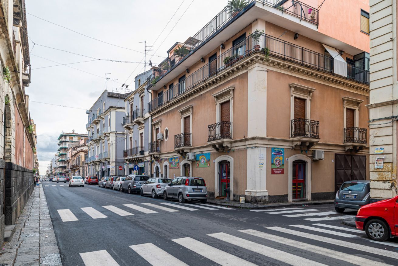 A street lined with multi-story buildings, parked cars, and a pedestrian crossing.