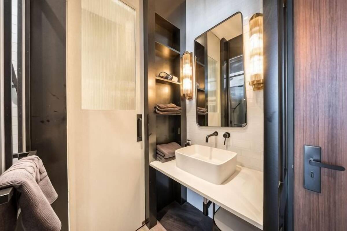 A modern bathroom with a large mirror, a white sink, and a towel rack.