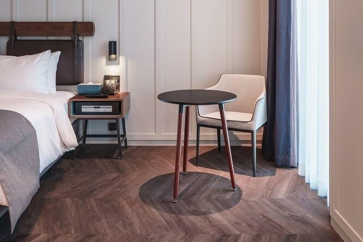 A hotel room with a bed, a small table, a chair, and a nightstand.
