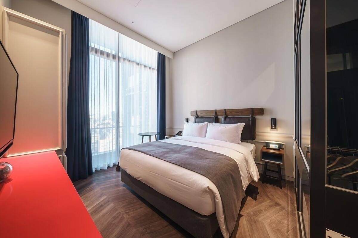 A hotel room with a large bed, a desk, a chair, a small table, and a wardrobe.