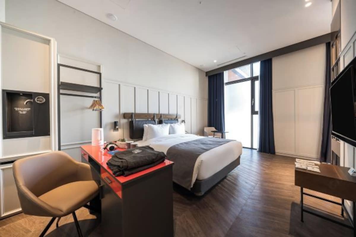 A modern hotel room with a bed, desk, chair, and TV.