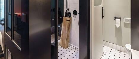 A modern bathroom with a shower, a toilet, and a sink. There is a wooden bench and a towel rack.