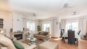 Una sala de estar amplia con chimenea, un comedor con mesa y sillas, y un gran ventanal con cortinas.