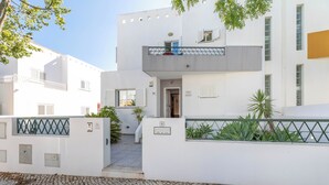 Un edificio moderno con techo plano, balcón y un área de entrada pavimentada.