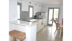 A modern kitchen with white cabinetry, a central island, and a dining area with a wooden table and chairs. - Traditional Cycladic house in the heart of Parikia with garden.  (Paros)