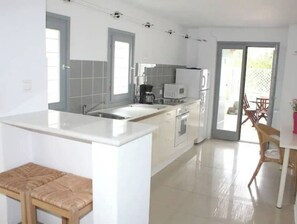 Una cocina moderna con muebles blancos, una isla central y un comedor con mesa y sillas de madera.