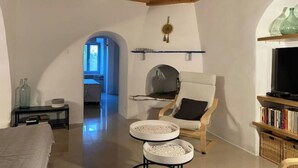 A spacious living room with a high ceiling, a fireplace, a comfortable armchair, a television, and a bookshelf. - Traditional Cycladic house in the heart of Parikia with garden.  (Paros)