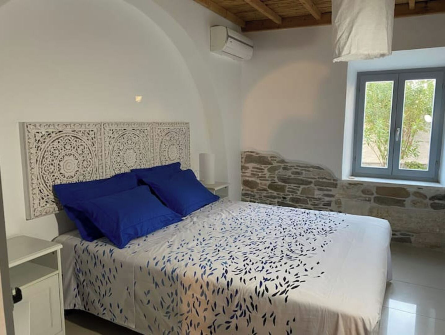 Ein Schlafzimmer mit einem Bett, einer Steinwand, einem Fenster und einer Klimaanlage.