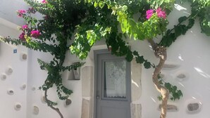 A white building with a gray door, potted plants, and a stone wall. - Traditional Cycladic house in the heart of Parikia with garden.  (Paros)