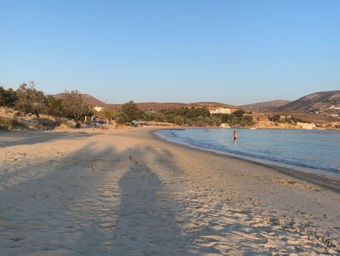 Una platja amb cel blau, sorra daurada i alguns edificis al fons.