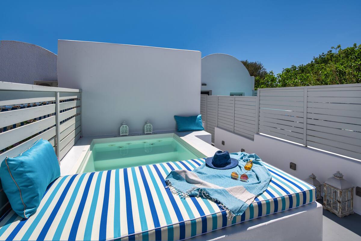 A rooftop terrace with a hot tub, striped cushions, and a hat.