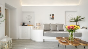 A modern living room with a white sofa, a wooden coffee table, and a vase of flowers. - Amoramelia Suites (Santorini)