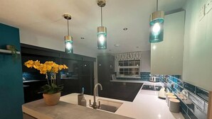 Een moderne keuken met een centraal eiland, hanglampen en een potplant.