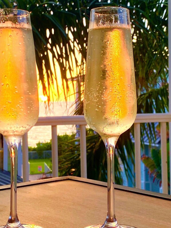 Two champagne flutes on a table with a view of a garden and a building in the background.