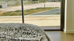 A room with a large window offering a view of a coastal landscape, a fluffy rug, and a tiled floor. - Ocean view Architectural Modern Villa (Luz)
